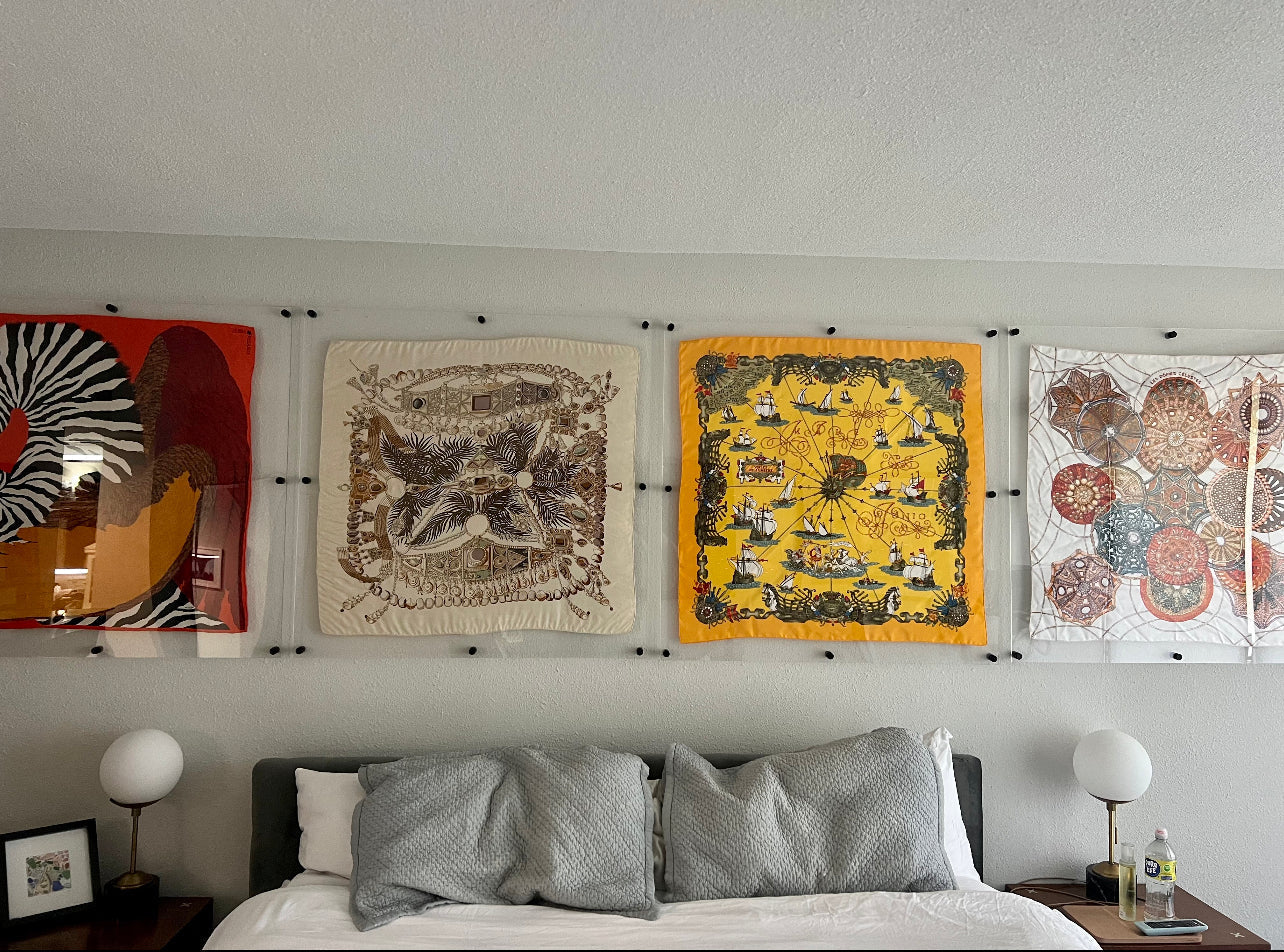 Gallery wall of large floating acrylic frames displaying framed silk scarves above a bed