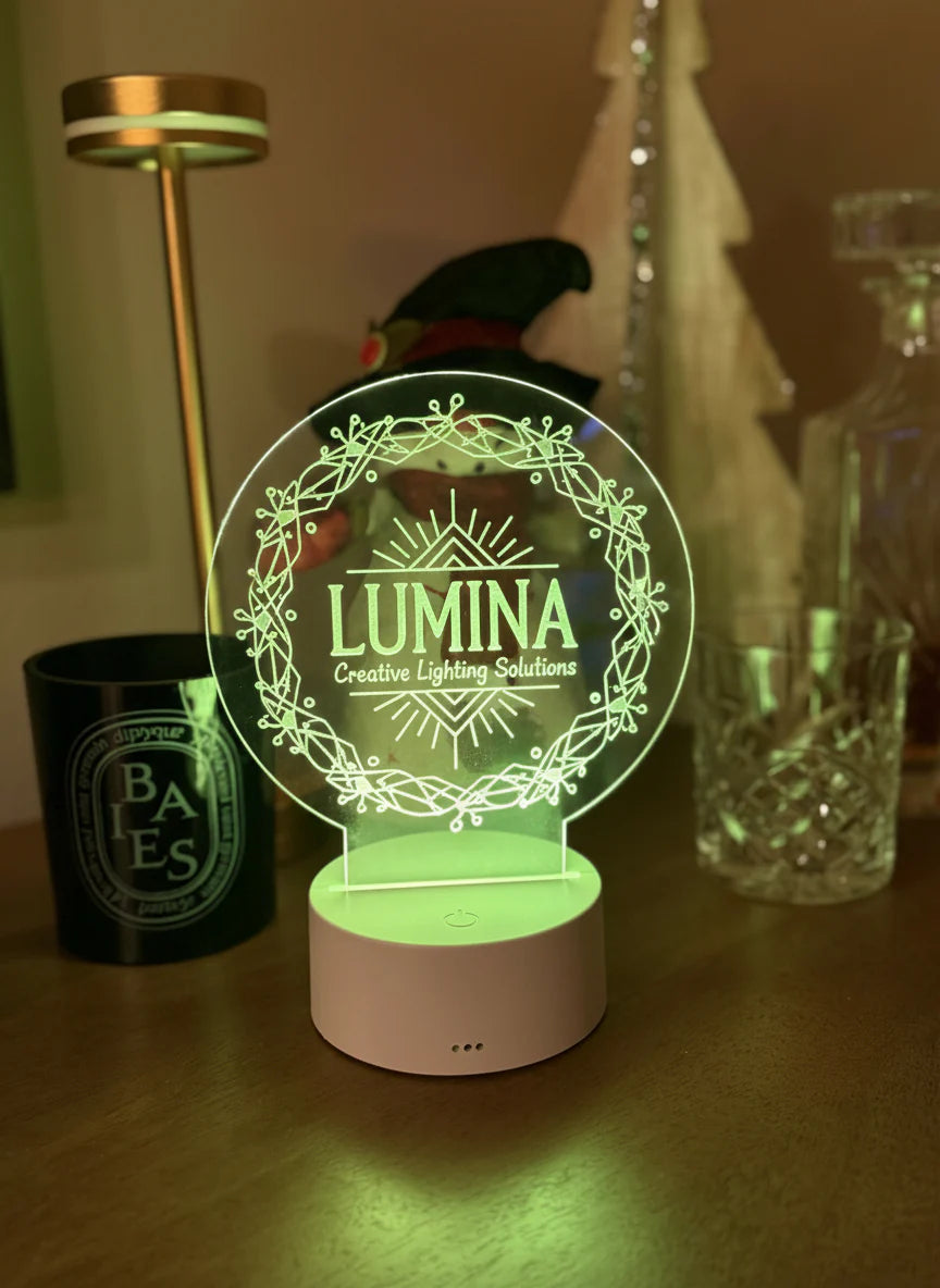 Round engraved acrylic LED table sign glowing green on a wooden base beside candles