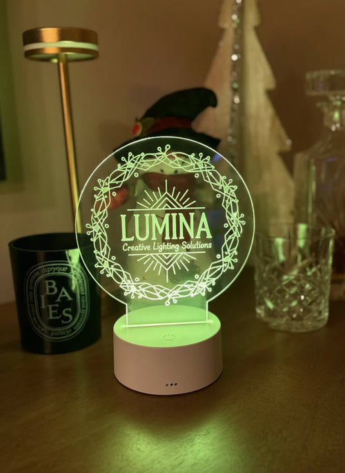Round engraved acrylic LED table sign glowing green on a wooden base beside candles