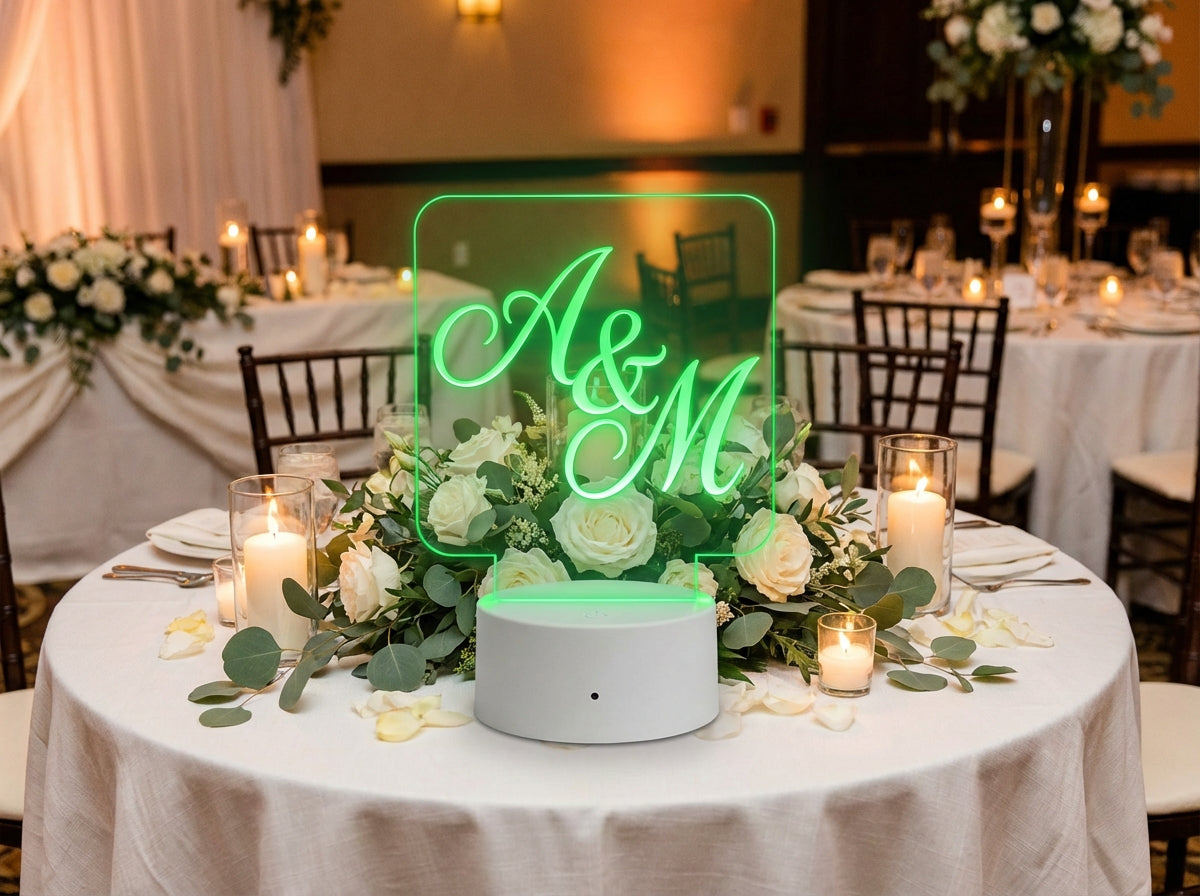 Acrylic LED sign engraved with wedding initials glowing green on a floral reception centerpiece