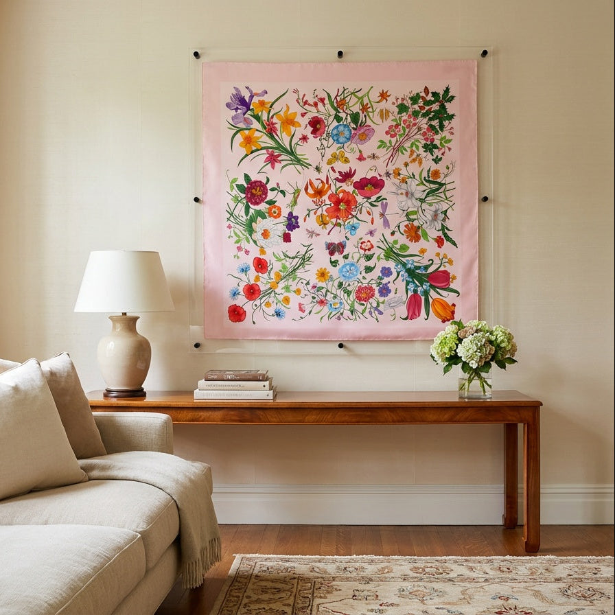 A large pink fabric wall hanging with a colorful floral and bird pattern, displayed in a styled living room above a wooden console table.
