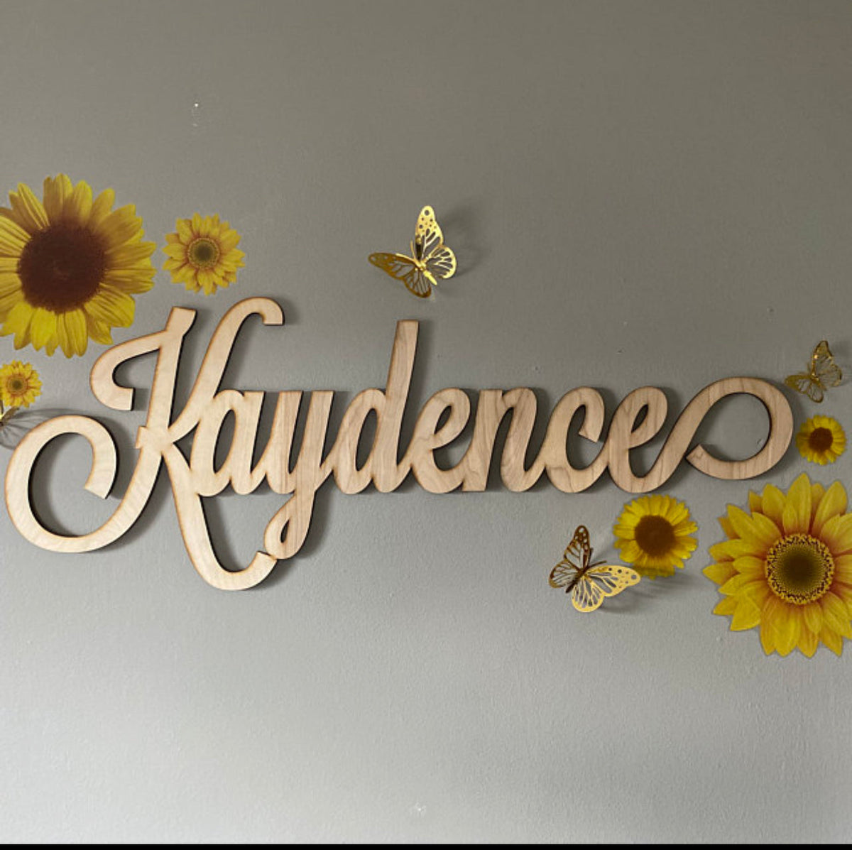 Custom wood name sign reading Kaydence in script lettering decorated with sunflowers and butterflies
