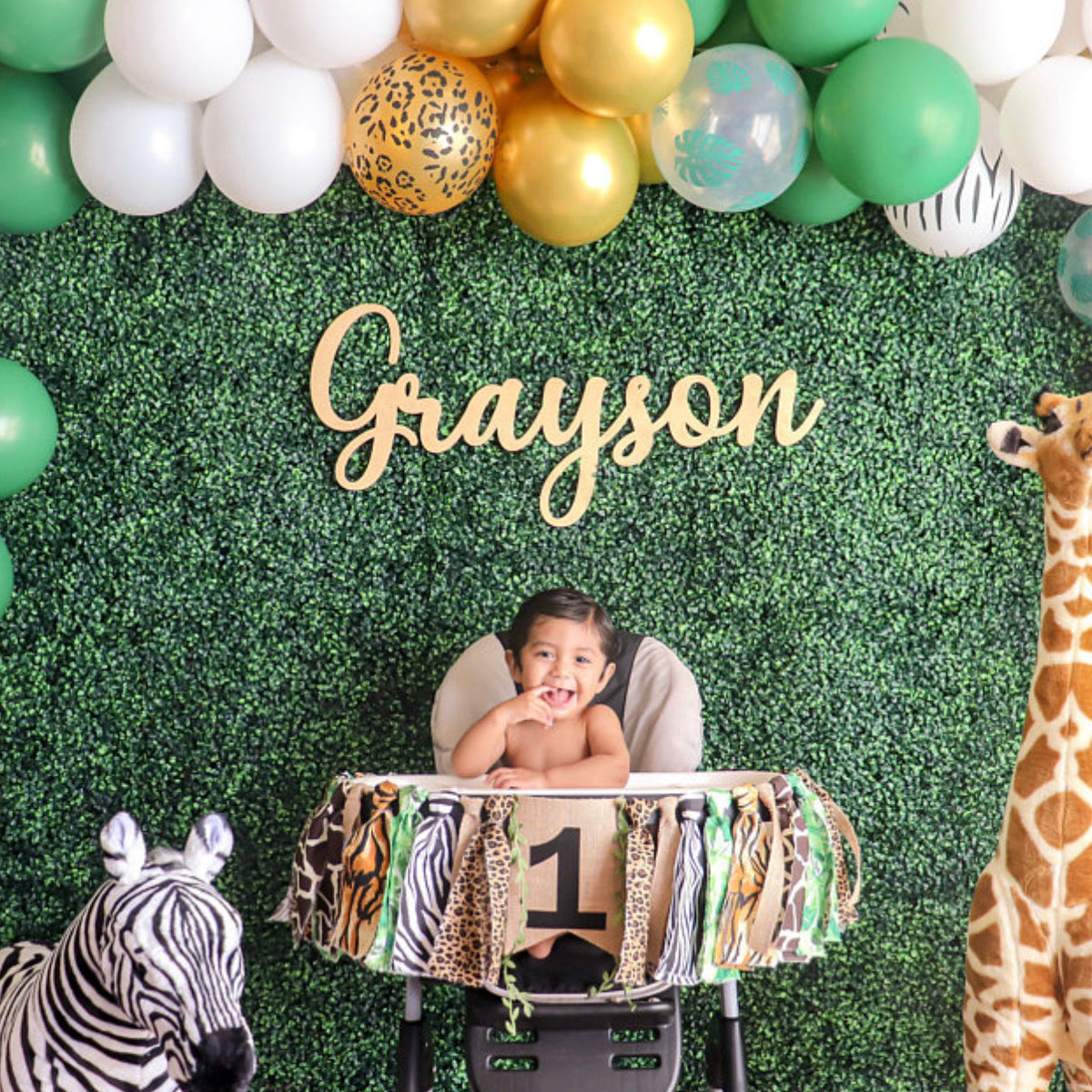 Custom wood name sign reading Grayson above a safari themed first birthday high chair setup