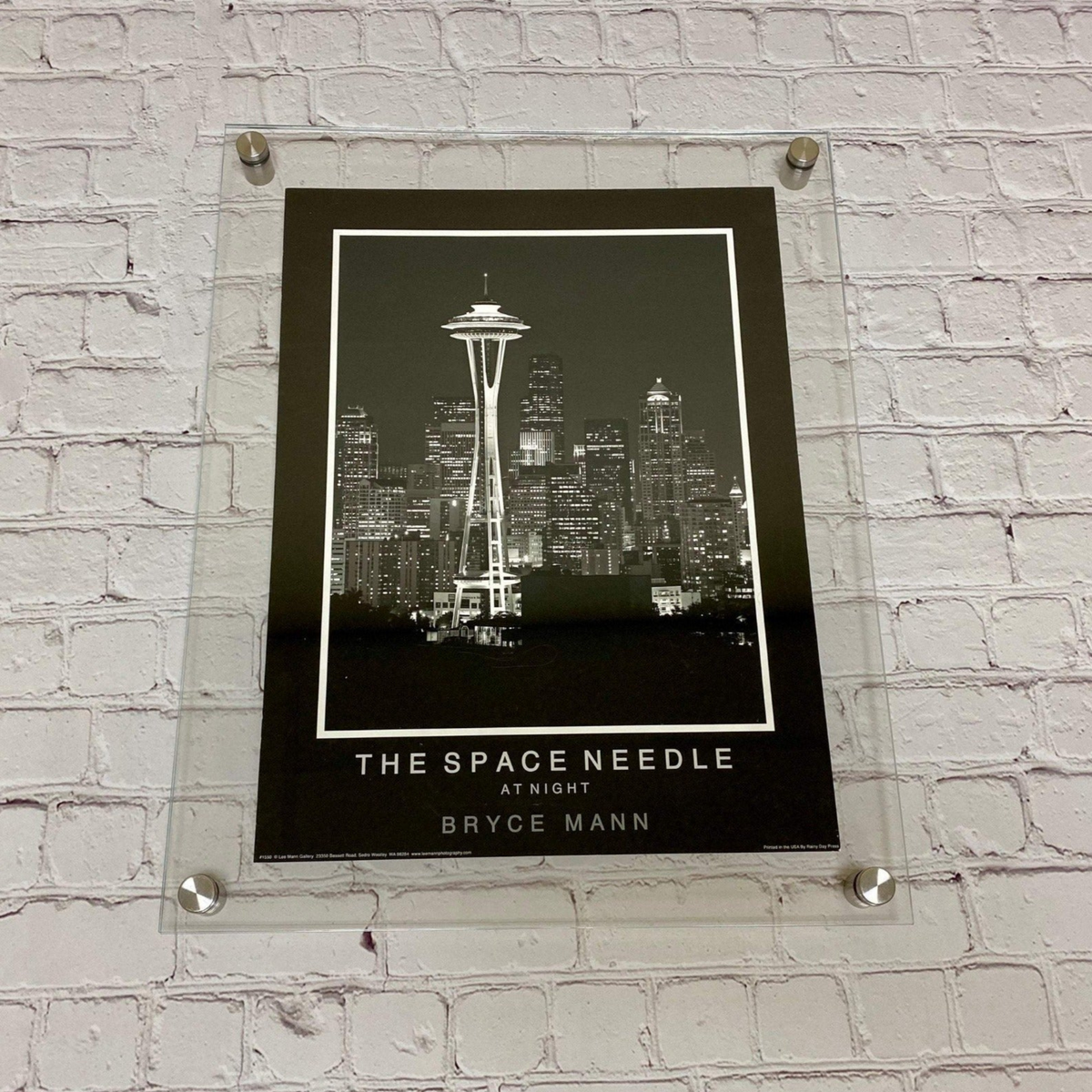 Clear floating acrylic picture frame with straight corners holding a Space Needle print on a white brick wall