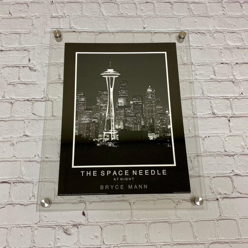 Clear floating acrylic picture frame with straight corners holding a Space Needle print on a white brick wall