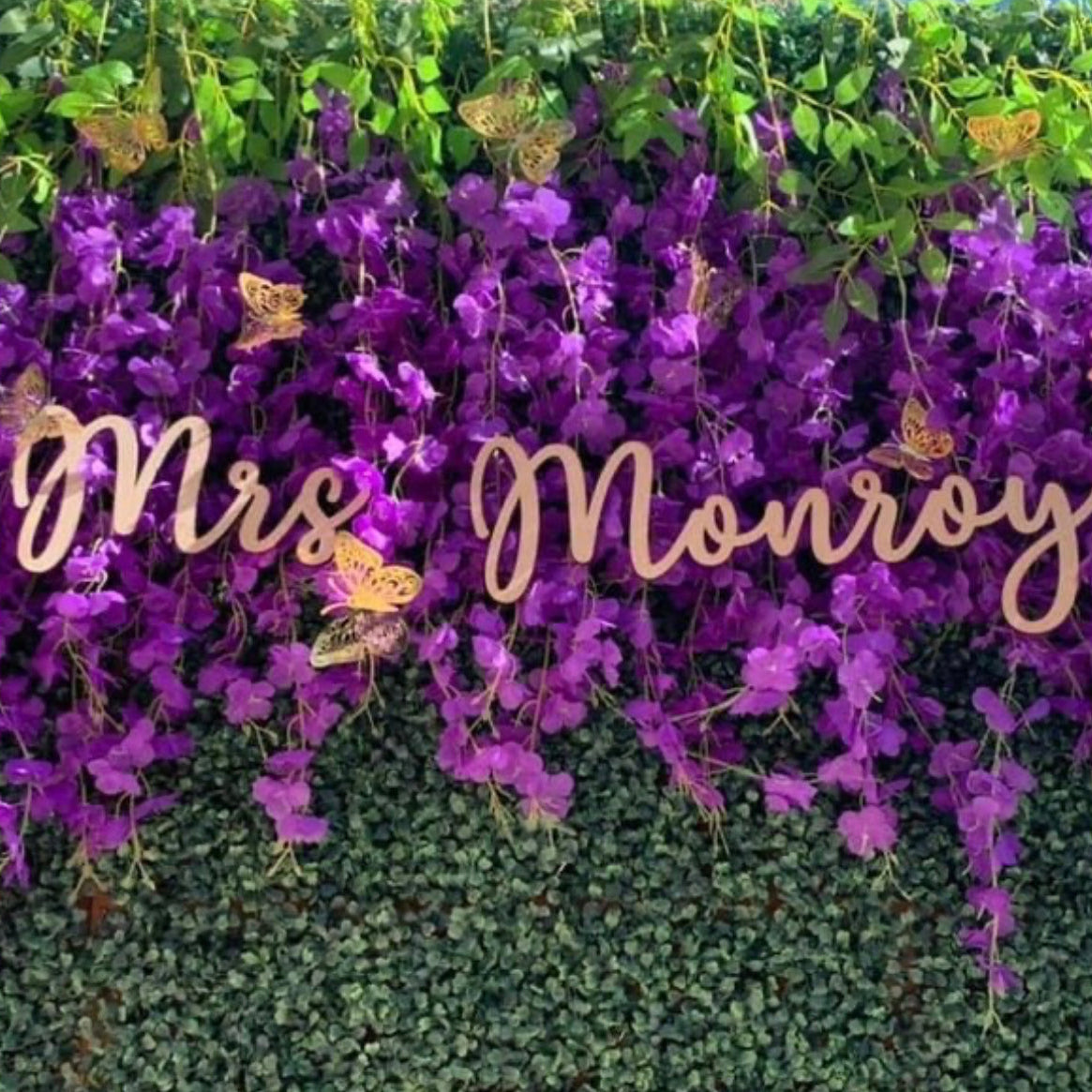 Custom wood sign reading Mrs Monroy in script lettering on a purple flower wall